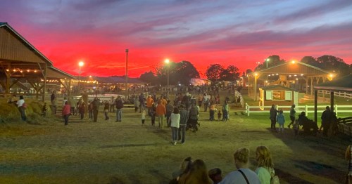 A vibrant sunset casts a colorful sky over a bustling fairground with people enjoying the evening.