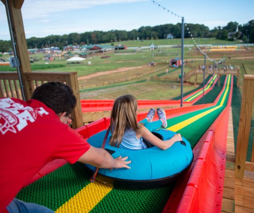 A child in a blue inner tube prepares to slide down a colorful water slide, with an adult assisting from behind.