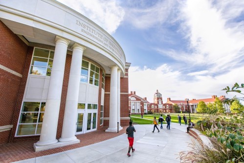 Students walk past the Institute of Engineering on a sunny day, with historic buildings and greenery in the background.