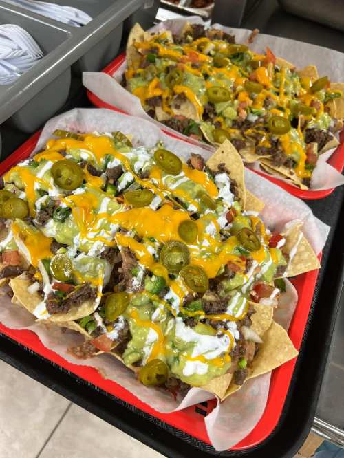 Two trays of loaded nachos topped with cheese, jalapeños, sour cream, guacamole, and diced tomatoes.