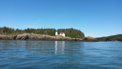 A serene coastal scene featuring a lighthouse on a rocky shore, surrounded by lush green trees under a clear blue sky.