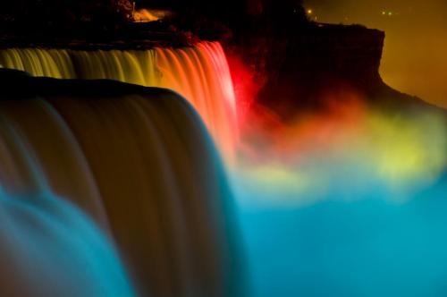 A vibrant view of illuminated waterfalls at night, showcasing colorful lights reflecting on the water.