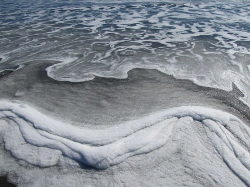 Foamy ocean waves gently rolling onto a sandy beach, creating intricate patterns on the water's surface.