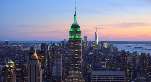 The Empire State Building illuminated in green at sunset, with the New York City skyline in the background.