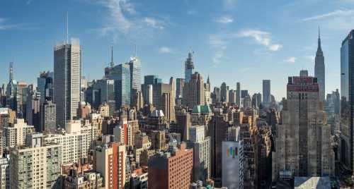 A panoramic view of a bustling city skyline featuring tall buildings and the Empire State Building under a clear blue sky.