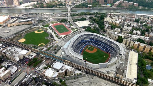 Aerial view of a baseball stadium surrounded by fields, buildings, and a river in the background.