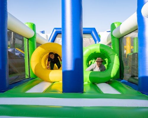 Two people play on a colorful inflatable obstacle course, crawling through large circular openings.