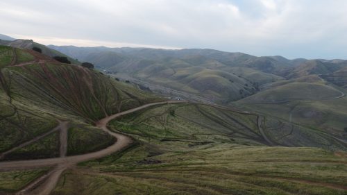 A panoramic view of rolling green hills and winding dirt paths under a cloudy sky.