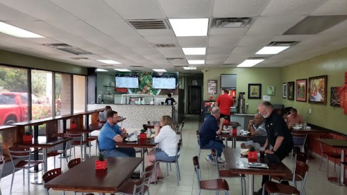 A casual restaurant interior with diners at tables, a counter in the background, and green walls adorned with art.