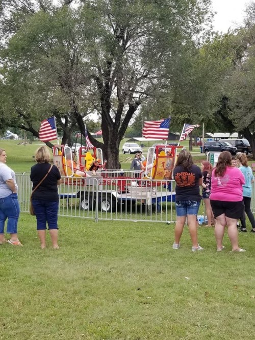 A group of people watching a small amusement ride decorated with American flags in a park setting.