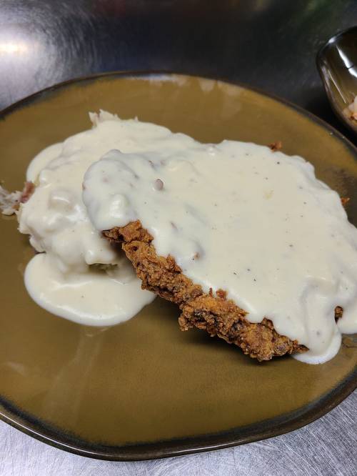 A plate with fried chicken covered in creamy white gravy, served alongside mashed potatoes.