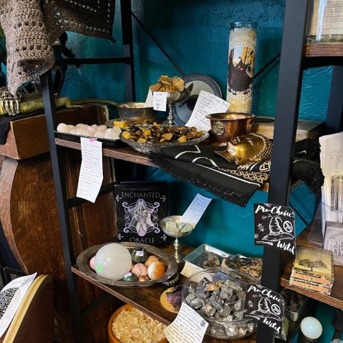 A display shelf filled with crystals, candles, and mystical items, featuring notes and an oracle deck.
