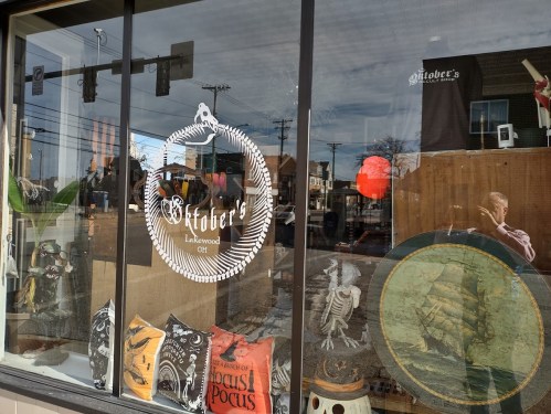 A storefront window displays decorative pillows, a sign for "October's" in Lakewood, and various items inside.