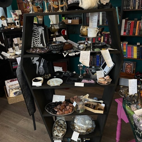 A black display shelf filled with various decorative items, crystals, and handwritten notes in a cozy shop setting.