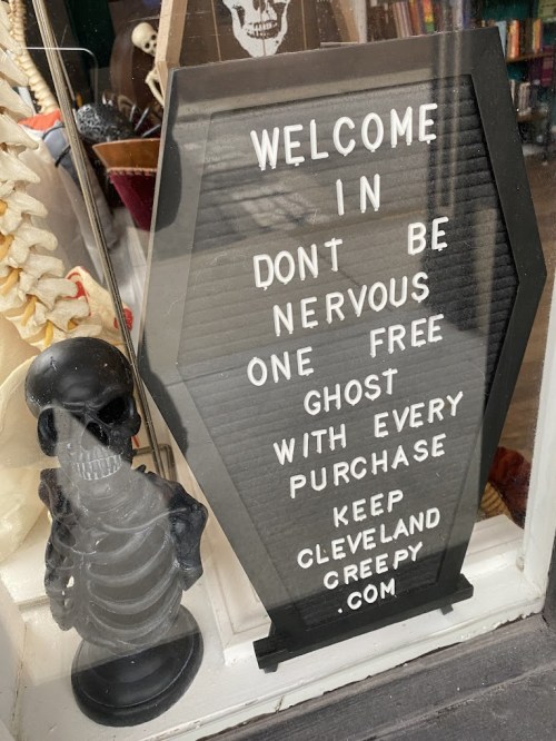 A sign in a shop window reads: "Welcome in. Don't be nervous. One free ghost with every purchase. Keep Cleveland creepy."