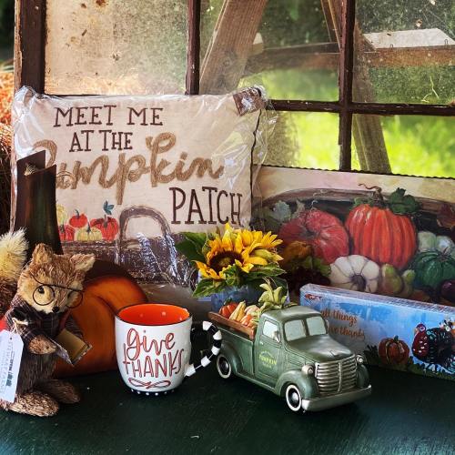A cozy fall display featuring a "Meet Me at the Pumpkin Patch" pillow, a truck planter, and autumn decorations.