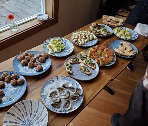 A table spread with various appetizers, including meatballs, oysters, and assorted bite-sized dishes on decorative plates.