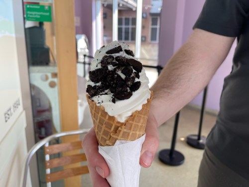 A hand holding a waffle cone filled with vanilla ice cream topped with crushed Oreo cookies.