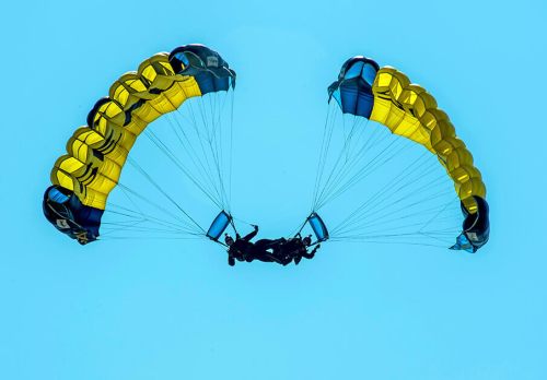 Two parachutists gliding through a clear blue sky with yellow and blue parachutes.