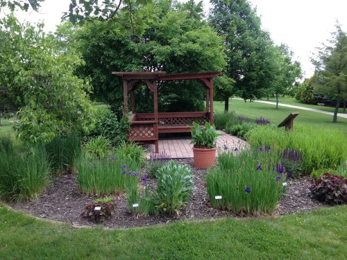 A wooden gazebo surrounded by lush greenery and colorful flowers in a serene garden setting.
