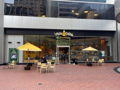 Exterior of Philz Coffee with outdoor seating and yellow umbrellas in a city plaza.