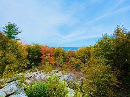 A scenic view of colorful autumn trees and rocky terrain under a blue sky with wispy clouds.