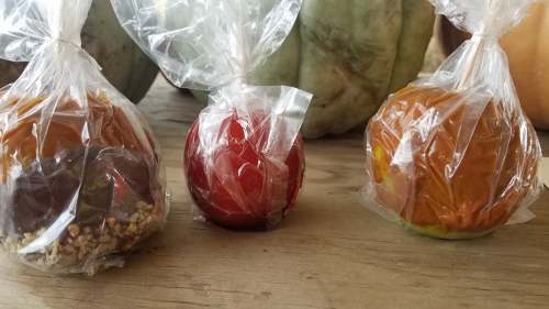 Three colorful candies wrapped in clear plastic, resembling small apples, placed on a wooden surface.