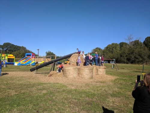 A group of children playing on a haystack with a slide, surrounded by a grassy field and inflatable attractions in the background.