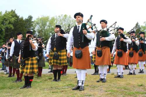 A group of bagpipers in traditional Scottish attire, including kilts and hats, performing outdoors.