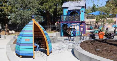 Colorful playground featuring a unique blue and orange play structure, a cozy hut, and children playing in a sunny park.