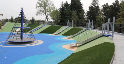 A colorful playground featuring slides, a climbing structure, and grassy hills under a cloudy sky.