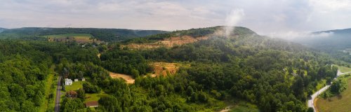 A panoramic view of lush green hills and valleys under a cloudy sky, with a road winding through the landscape.