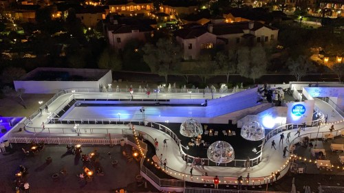 Aerial view of a vibrant outdoor venue with illuminated pools, people skating, and cozy seating areas at night.
