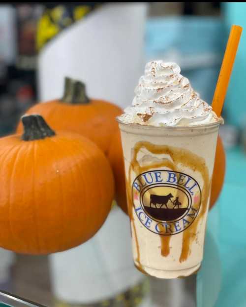 A creamy pumpkin-flavored milkshake topped with whipped cream and caramel, next to two pumpkins.