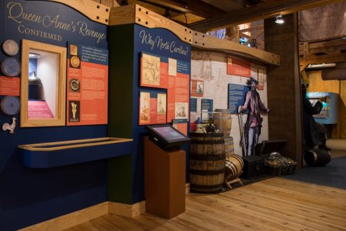 Exhibit display featuring information about "Queen Anne's Revenge" with artifacts and interactive screens in a museum setting.