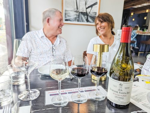 A couple enjoys a meal at a restaurant, smiling with wine glasses and a bottle on the table.