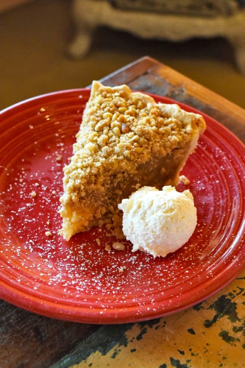 A slice of pie with a crumbly topping on a red plate, accompanied by a scoop of vanilla ice cream.