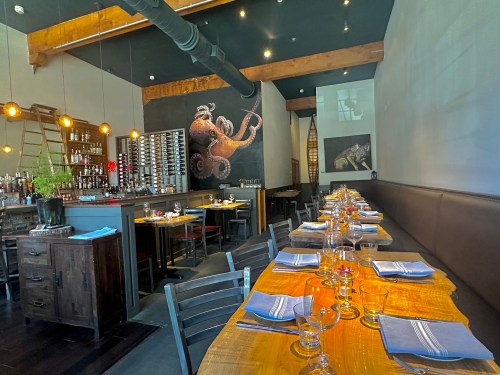 A modern restaurant interior featuring wooden tables, a bar, and artistic wall murals, with elegant table settings.