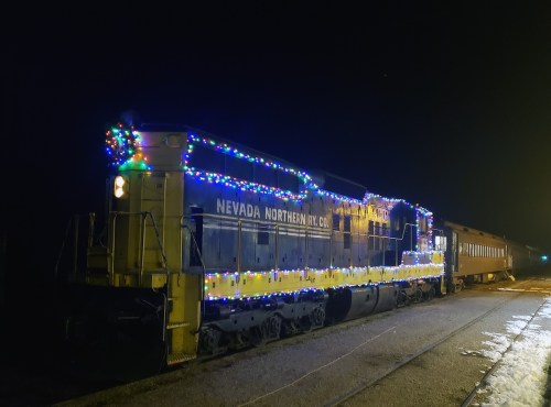 A brightly lit train decorated with colorful lights, parked on a track at night.