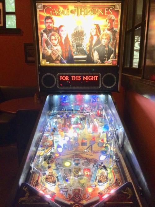A Game of Thrones pinball machine with vibrant lights and characters from the series displayed on the backboard.