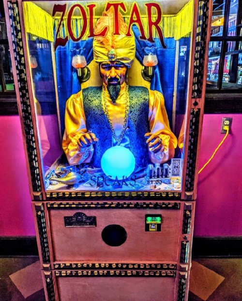 A fortune-telling machine named Zoltar, featuring a mystical figure with a crystal ball, set in a colorful arcade.