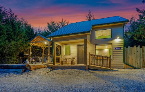 A cozy cabin with a porch, surrounded by trees, under a colorful sunset sky.