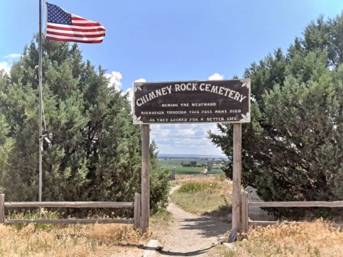 Sign at the entrance of Chimney Rock Cemetery, with an American flag and a view of the landscape beyond.