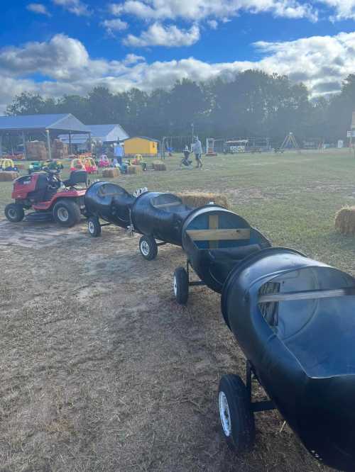 A row of black barrels on wheels, used as a train ride, with a tractor nearby and a farm setting in the background.