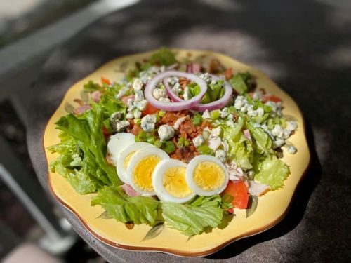 A colorful salad with greens, tomatoes, bacon, blue cheese, red onion, and sliced hard-boiled eggs on a yellow plate.