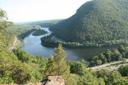 A scenic view of a winding river surrounded by lush green hills and trees under a clear blue sky.