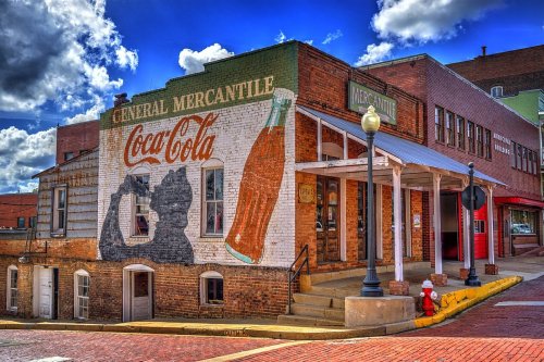 Historic building with a Coca-Cola mural, featuring a silhouette, on a sunny day with blue skies and clouds.