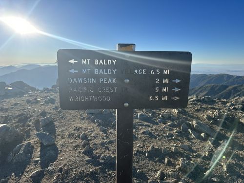 Signpost on a mountain trail indicating distances to Mt. Baldy, Dawson Peak, Pacific Crest Trail, and Wrightwood.
