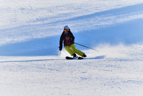 A skier in bright yellow pants and a black jacket gracefully carves through fresh snow on a sunny day.
