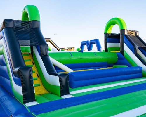 Colorful inflatable slides and obstacle course in a sunny outdoor setting.